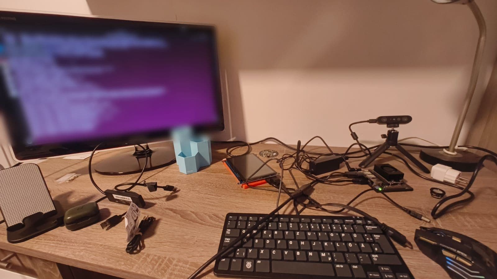 A desk with a monitor, a keyboard, the Jetson with its green power light, the 7 inch screen lying flat and the depth camera on its tripod.